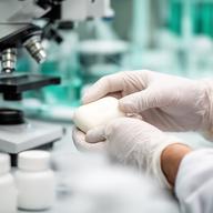 Responsable de calidad analizando muestras de jabón con instrumental de laboratorio y guantes blancos